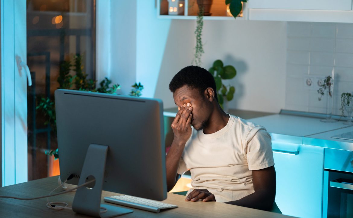 Overworked african man freelancer feeling eye strain and fatigue during prolonged computer use