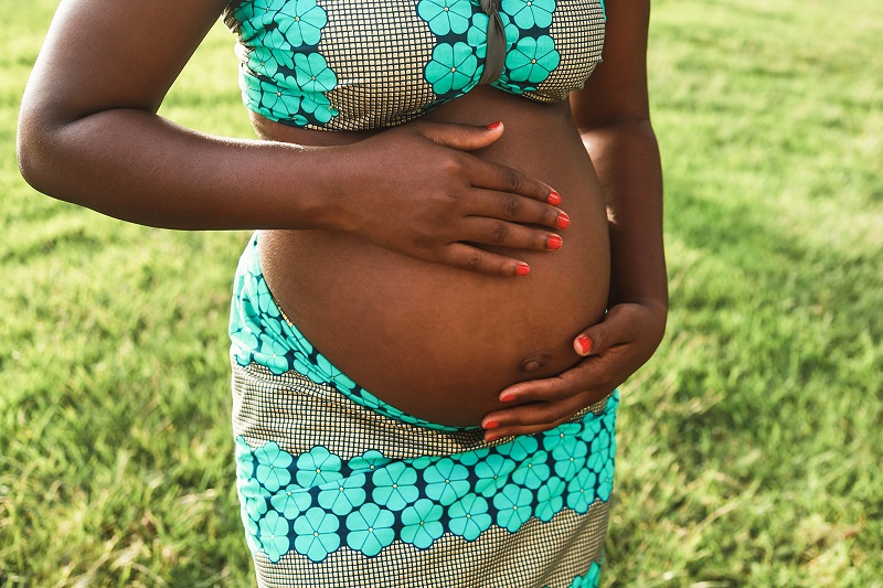 Young african pregnant woman having tender moment touching her belly outdoor - Focus on top hand