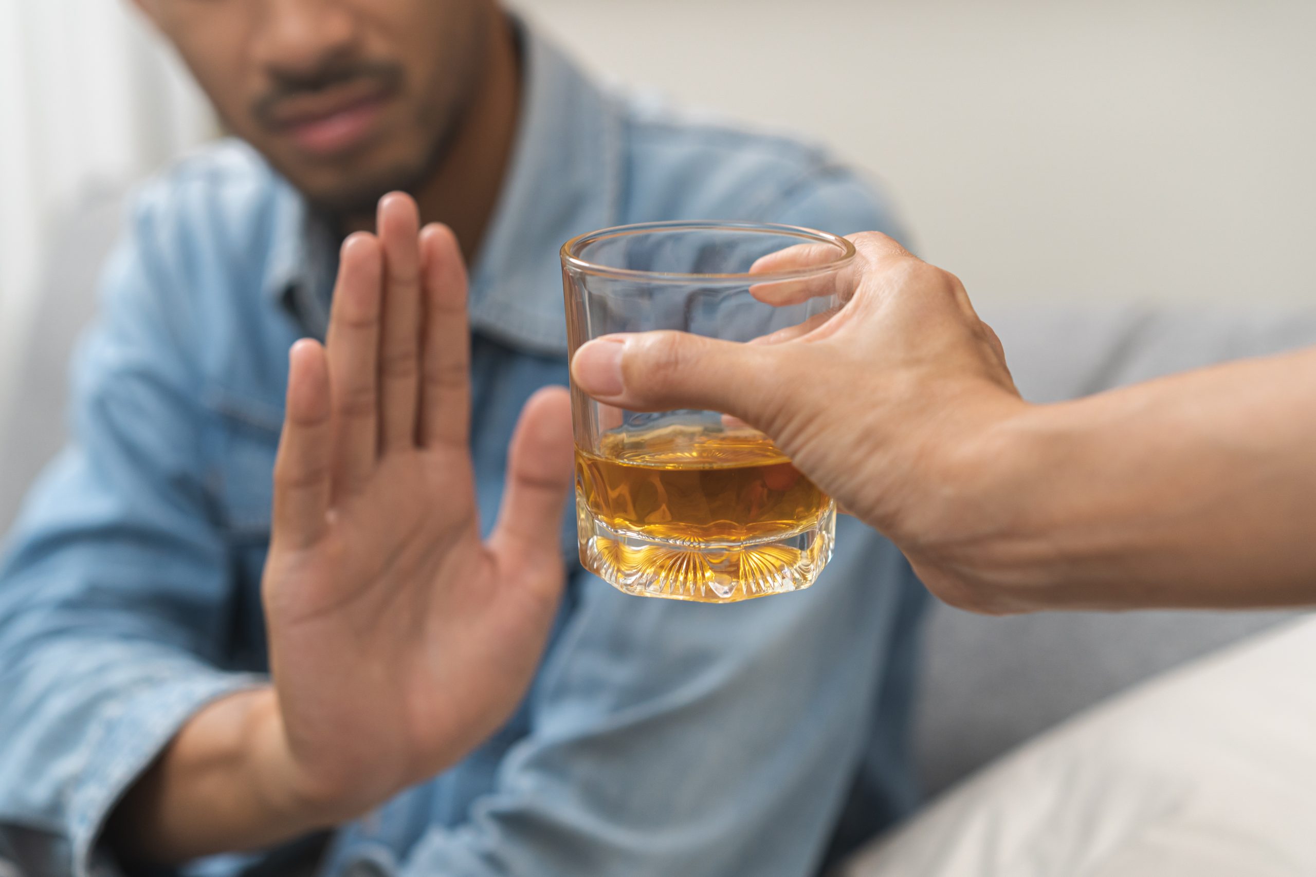 Alcoholism, depressed asian young man refuse, push out alcoholic beverage glass, drink whiskey, sitting alone at night. Treatment of alcohol addiction, having suffer abuse problem alcoholism concept.